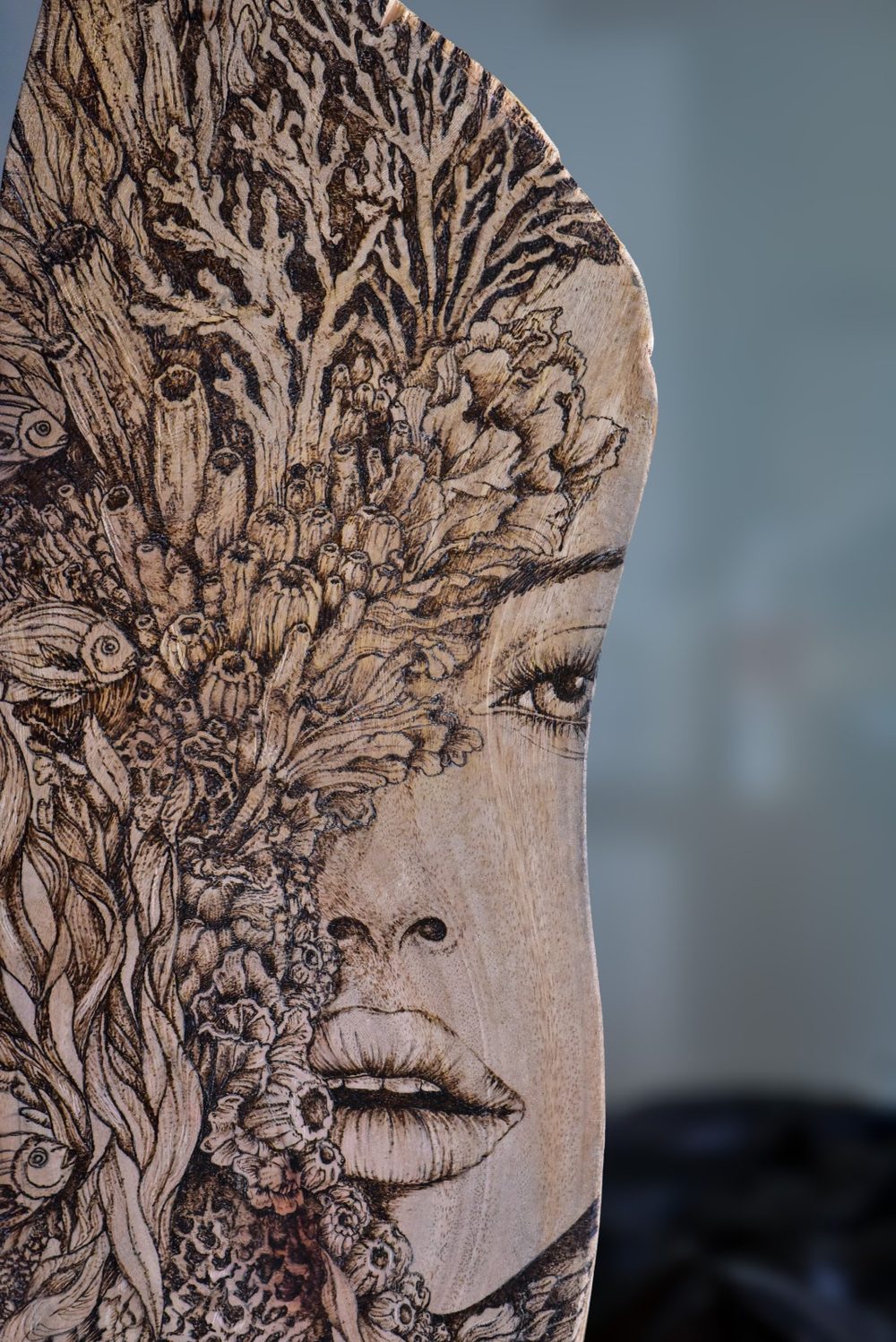 Detail of Still Becoming — burned coral and reef textures dissolving into a woman's face